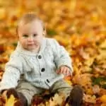 baby in sweater sitting on autumn leaves